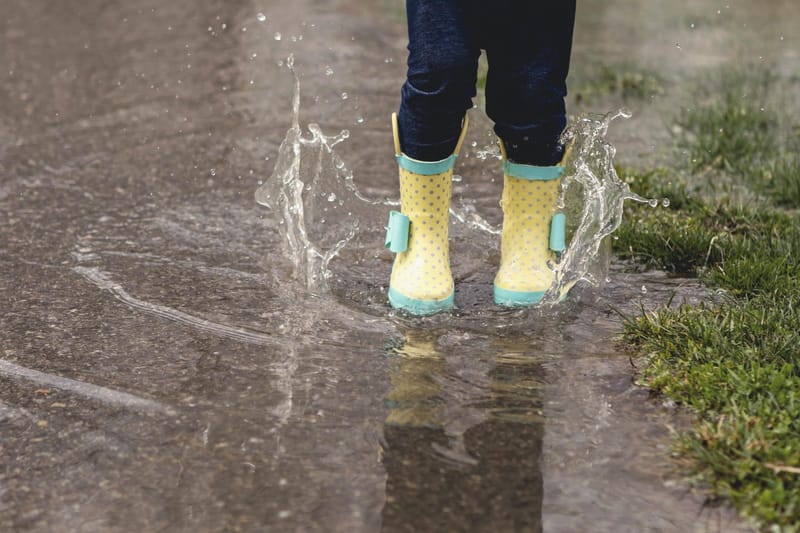 Child splashing in puddle wearing rainboots