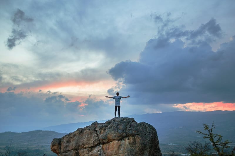 Man standing on a mountain with arms outstretched and blue sky before him